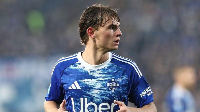 Soccer player in a blue kit, looking to the right on a football pitch, wet hair and determined expression, Uber logo on jersey