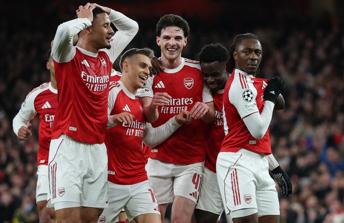 Arsenal players celebrate a goal on the pitch in red and white kits with smiles and hugs.