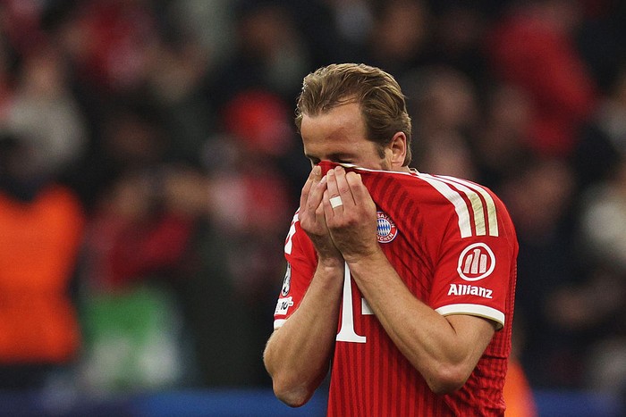 Professional footballer in a red Bayern Munich jersey covers his face with his shirt, likely disappointed on the field.