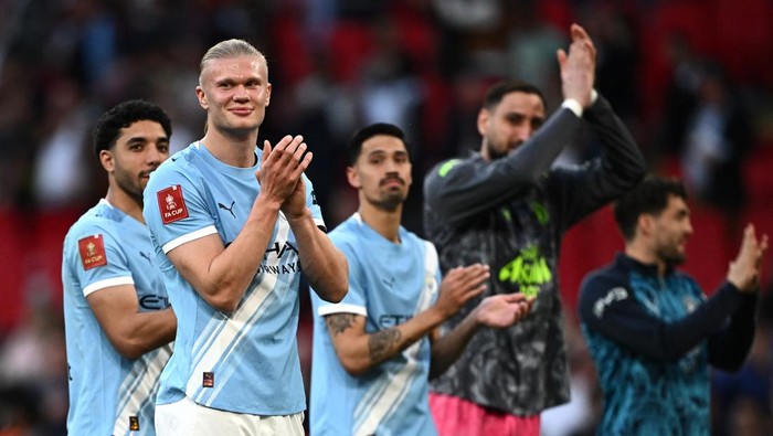Group of Manchester City players applauding on the pitch after a match in light blue kit.