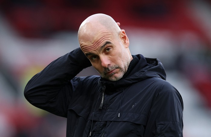 Bald man in a dark jacket touching the back of his neck, looking toward the camera with a puzzled expression.
