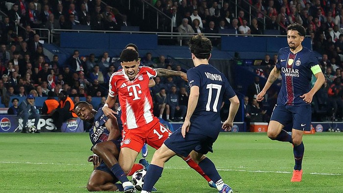 Soccer match action: a Bayern Munich player in red-and-white tries to win the ball while a defender in dark blue slides in, with another blue-clad player watching nearby.