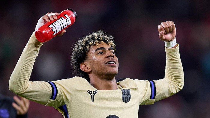 Soccer player celebrating on the field, holding a red Gatorade bottle aloft with his left arm while raising a clenched right fist.
