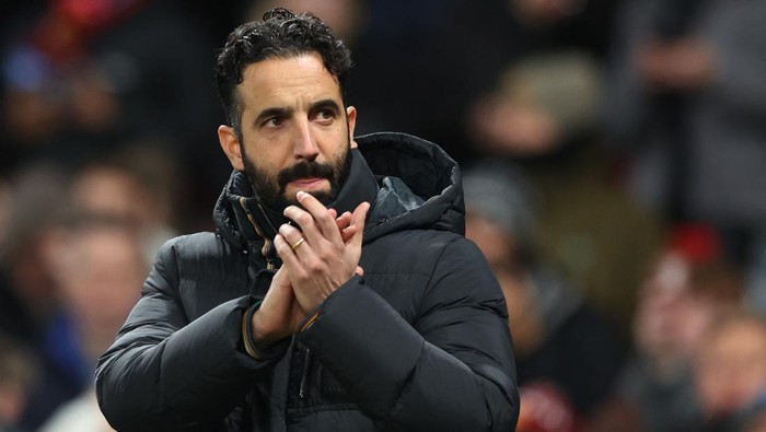 Bearded man in a black puffer jacket clapping during a sports event at the stadium.