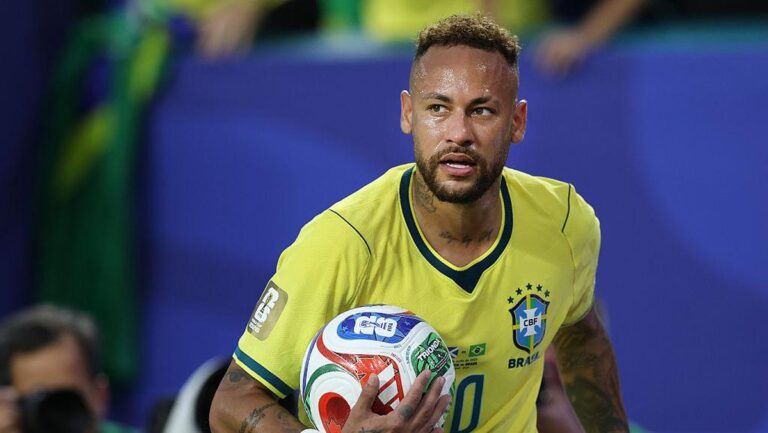 Brazilian footballer in a yellow Brazil kit holding a soccer ball on the pitch in a match
