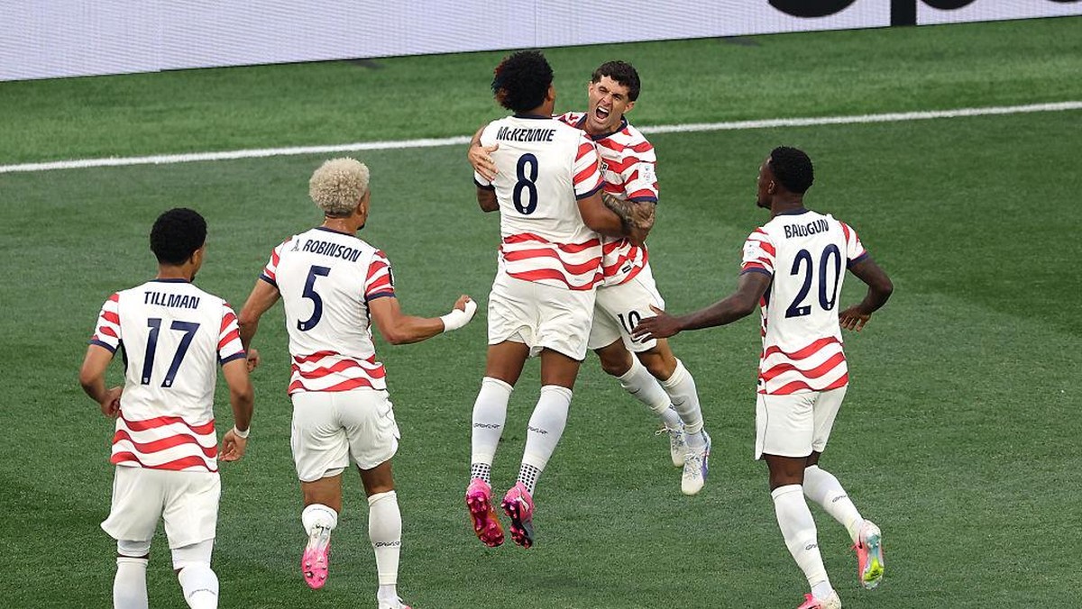 Soccer players in white and red striped jerseys celebrate on the field, jumping together after a goal.