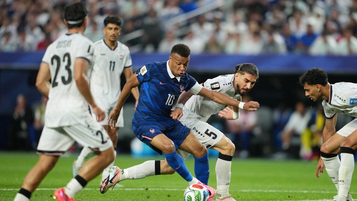 Soccer match action: a blue-jersey player (number 10) shields the ball from white-jersey defenders in a crowded field.