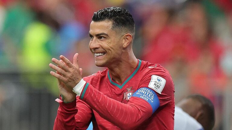 Portuguese soccer player in a red jersey clapping on the field during a match.