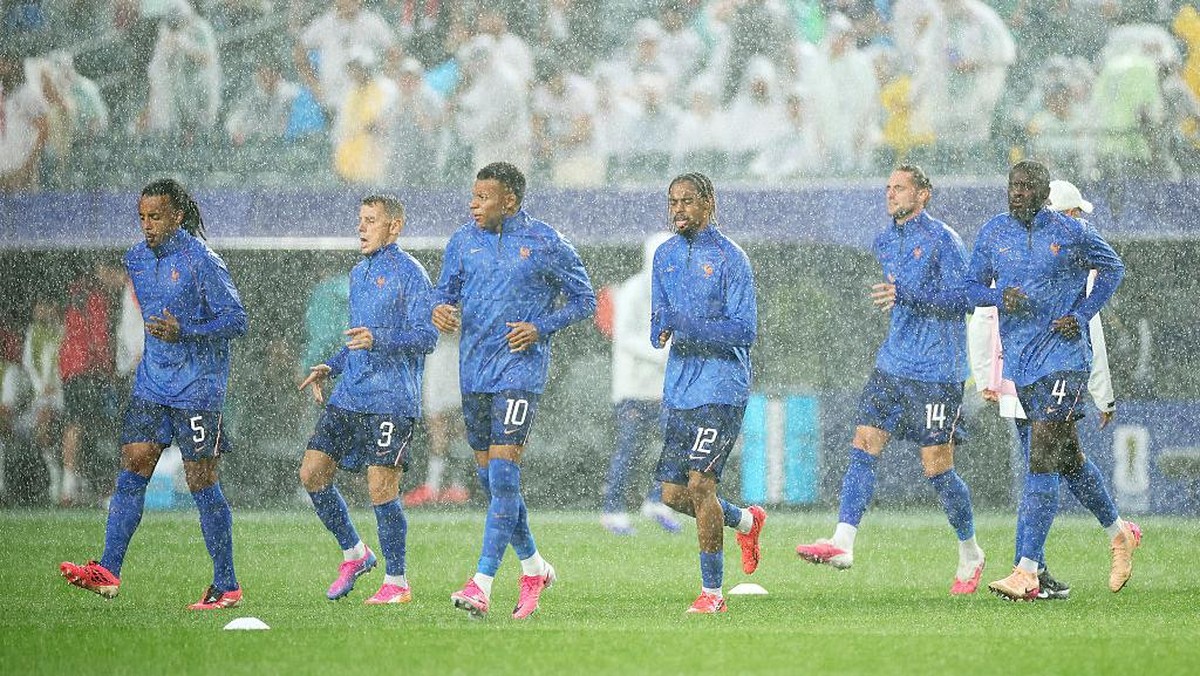 Soccer players in blue training outfits jog on a rainy pitch.