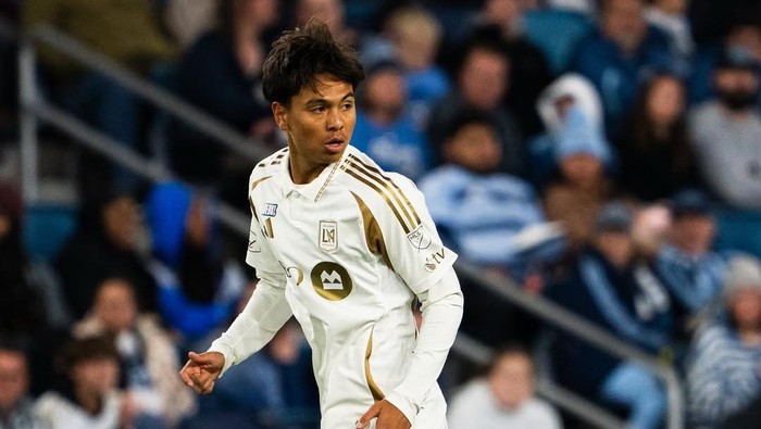 Soccer player in a white kit with gold stripes running on the field during a match.