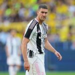 Soccer player in a black-and-white Juventus jersey on the field, looking toward the camera.