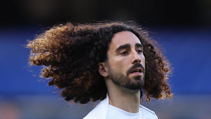 Man with long curly hair blowing in the wind, wearing a white shirt outdoors.