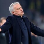 Soccer manager on the touchline with arms outstretched during a match, signaling or arguing a call.