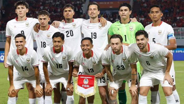 Indonesia men’s national football team posing for a group photo on the field, wearing white jerseys with numbers; goalkeeper in green stands at the back.