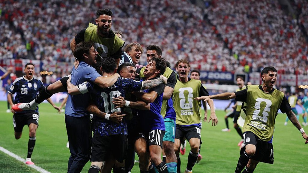 Soccer players hug and celebrate on the field as fans cheer in the packed stadium behind them.