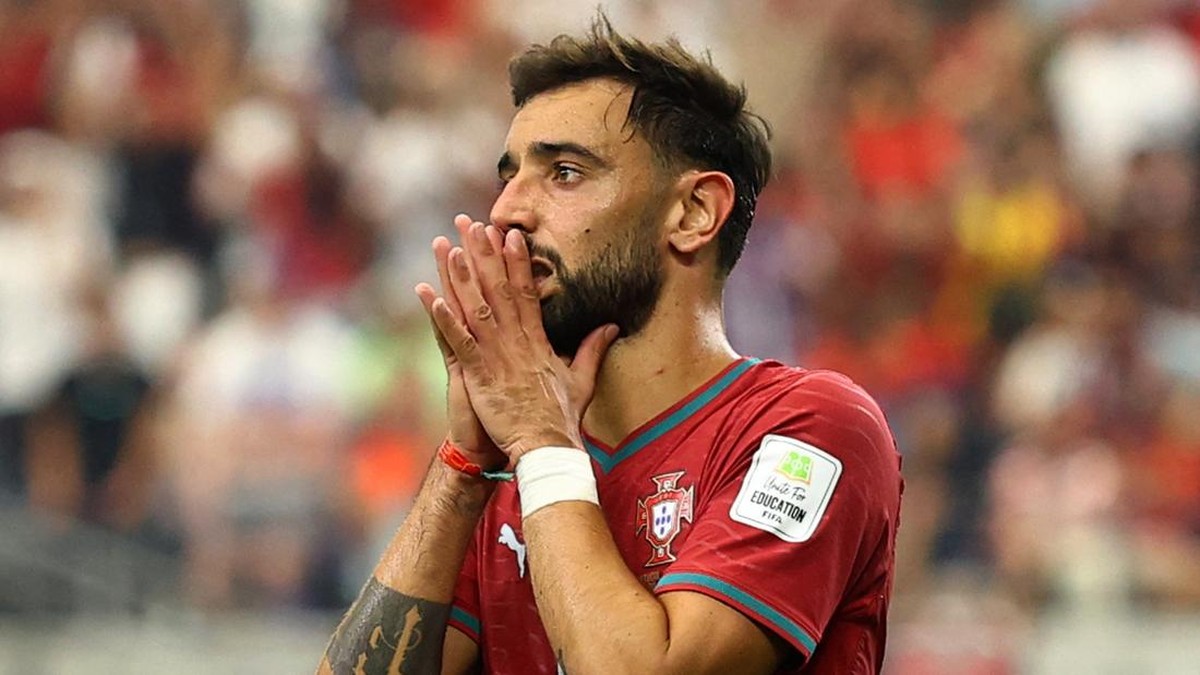 Portuguese footballer in a red jersey with hands to his mouth, showing emotion on the field amid a cheering crowd.