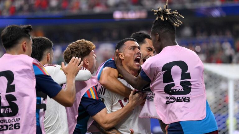 Soccer players in pink bibs celebrate a goal, with shouts and hugs on the field.
