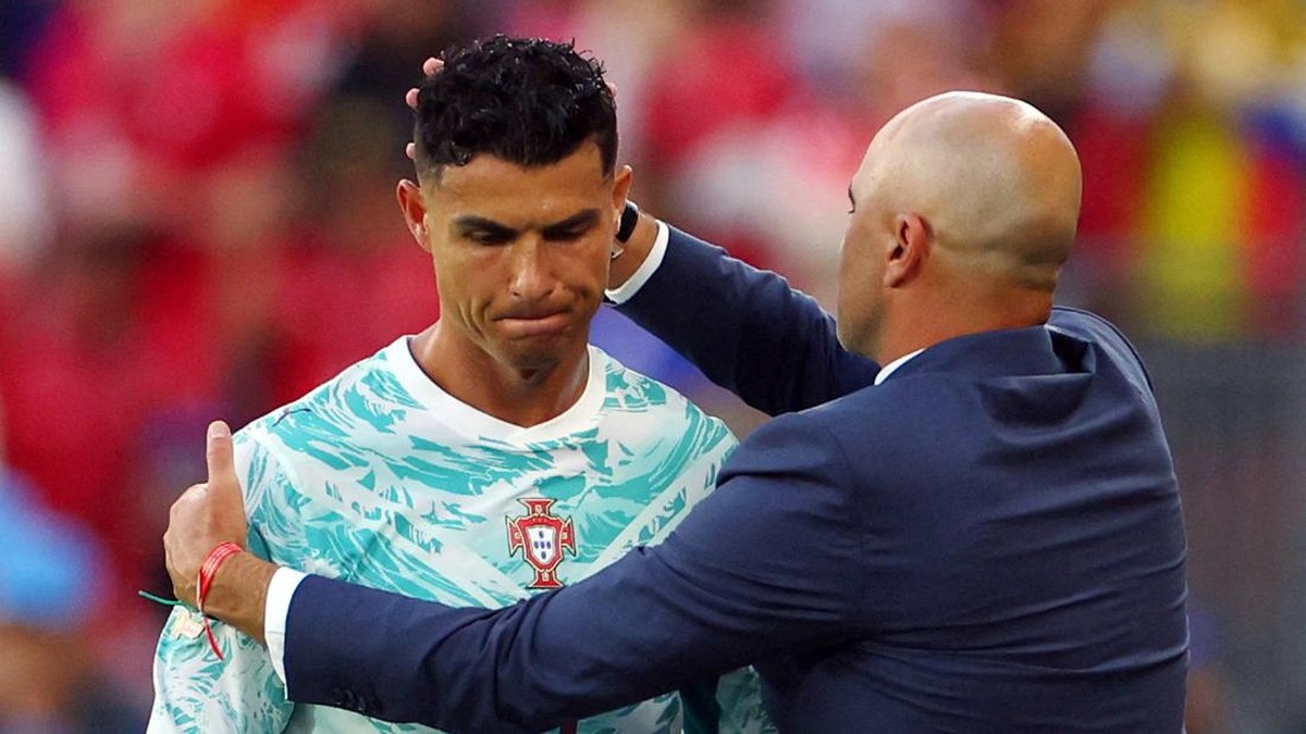 Coach consoles a soccer player by placing a hand on his head and shoulder during a match, both in focus on the field badge visible on jersey.