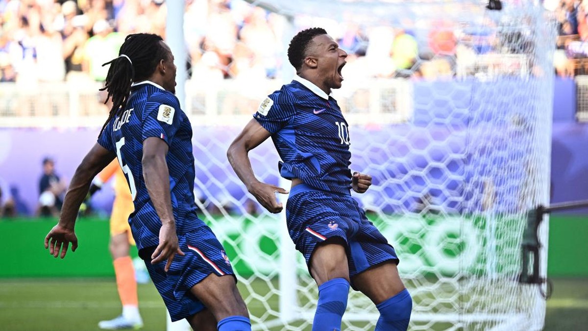 Two soccer players in blue jerseys celebrate a goal near the net, crowd cheering in the background