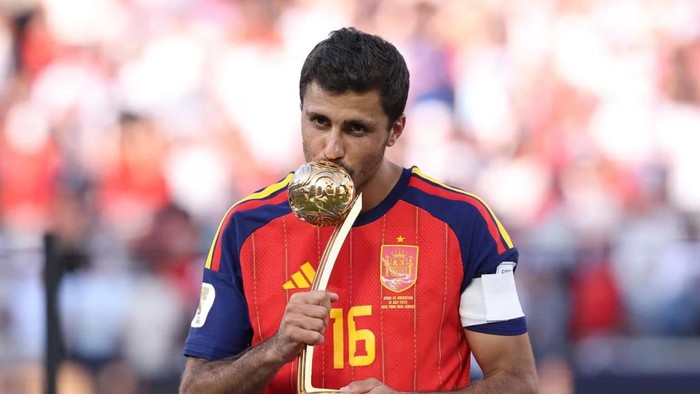 Soccer player in a red Spain jersey kissing the FIFA World Cup trophy on the pitch