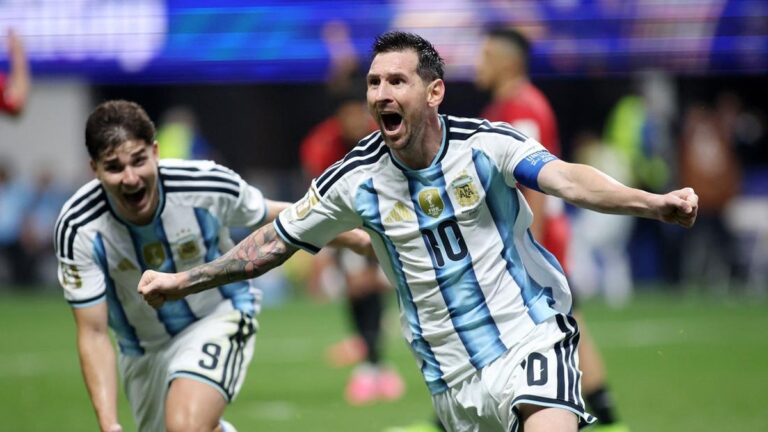 Argentina captain Lionel Messi (number 10) celebrates a goal with a teammate on the soccer field, arms raised in jubilation, wearing blue-and-white stripes.