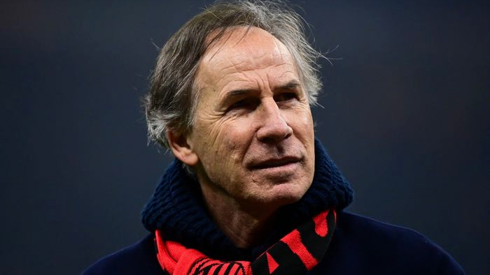 Portrait of an older man with gray hair, wearing a dark coat and a red-and-black scarf, looking to the side.