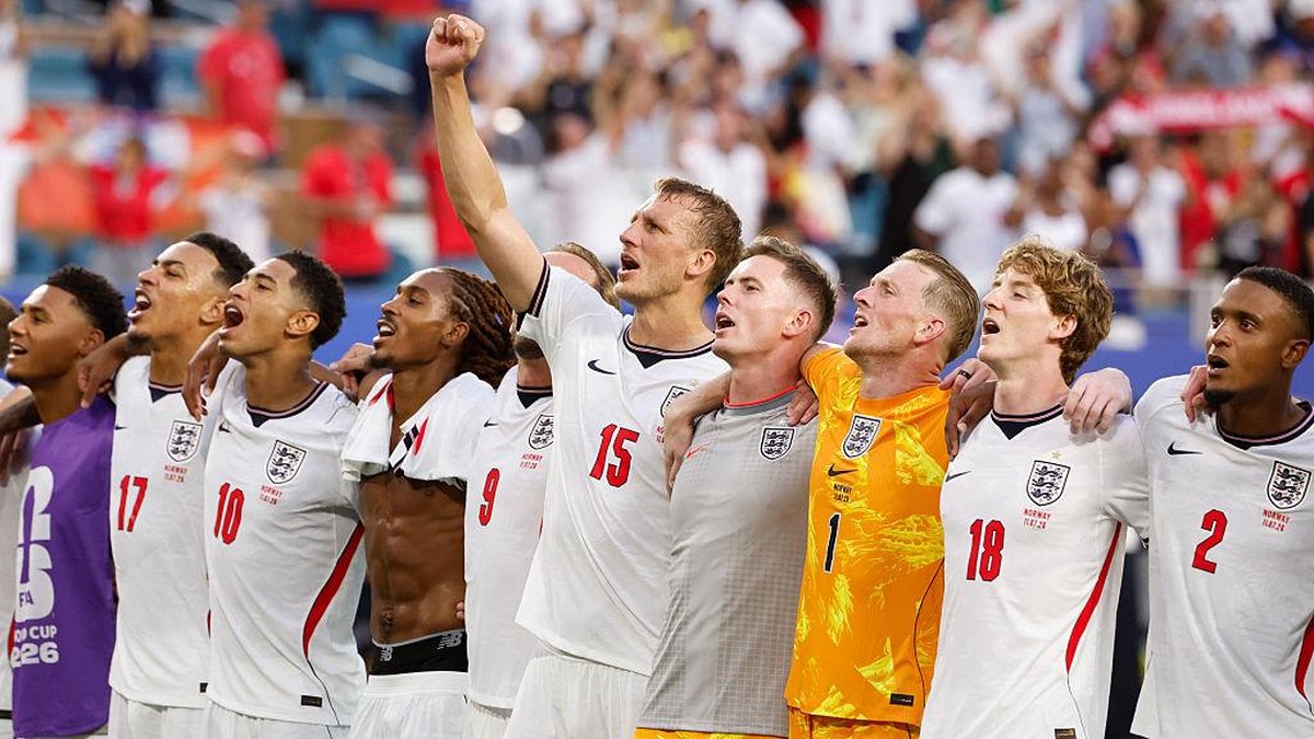 England national football team players stand arm-in-arm, one raising a fist in celebration on the pitch.