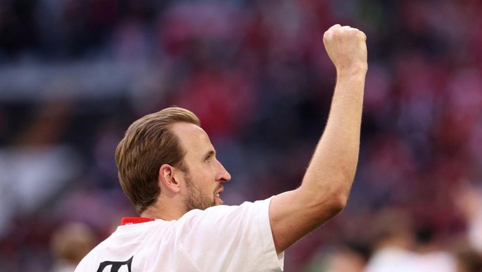 Male soccer player in a white jersey raises his fist in celebration on the field.
