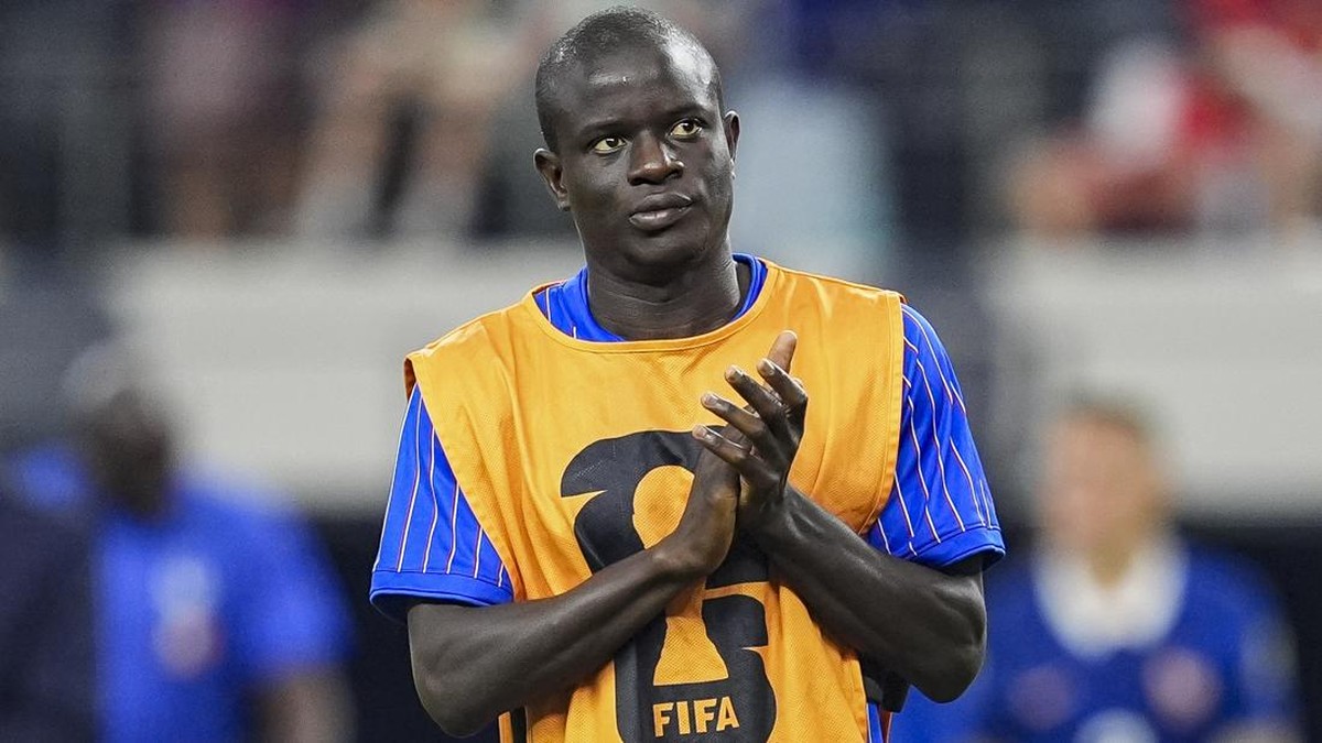 Football player wearing an orange bib with a FIFA logo stands on the field, hands held together in a prayer-like gesture.