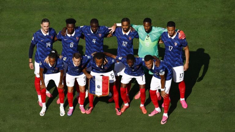 France national football team in blue jerseys huddled together on a grass field, arms around teammates for a pre-match photo.