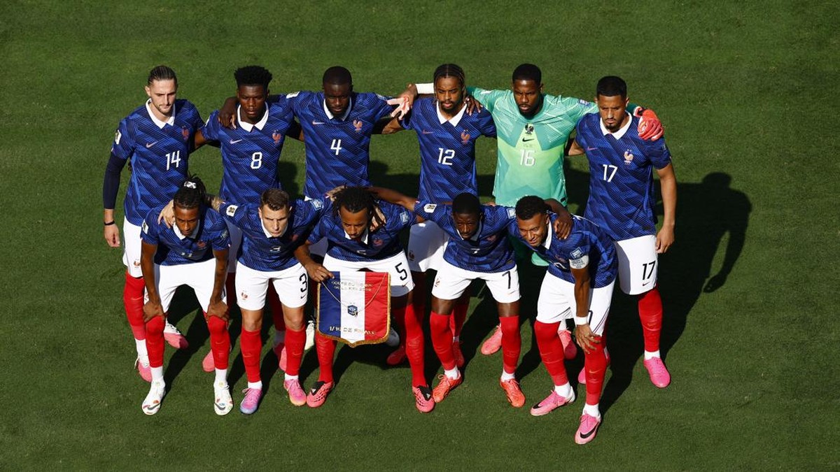 France national football team in blue jerseys huddled together on a grass field, arms around teammates for a pre-match photo.