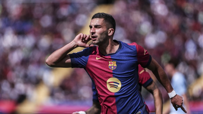 Soccer player in a Barcelona jersey celebrating a goal, with hand cupped to ear as the crowd cheers in the background