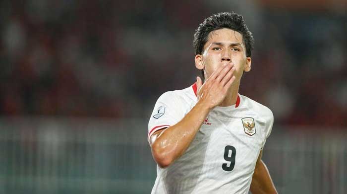 Soccer player in a white jersey with the number 9 celebrating by blowing a kiss to the crowd.
