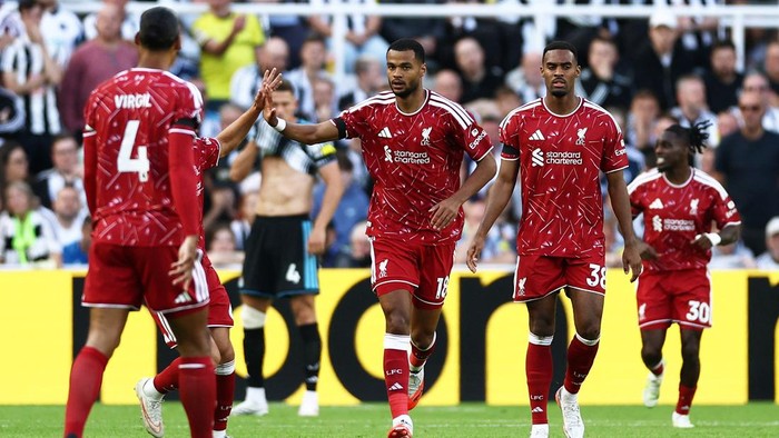 Liverpool players in red kits high-fiving on the soccer pitch during a match, celebrating a moment together.