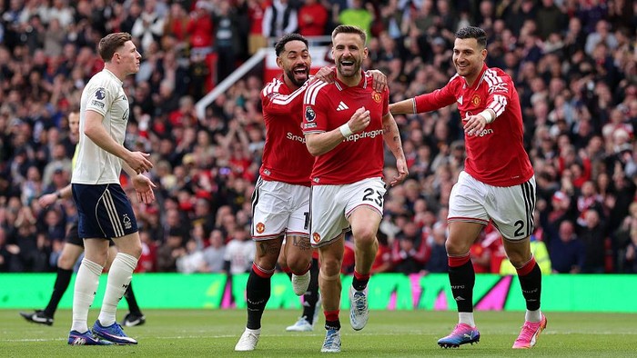 Manchester United players in red celebrate a goal on the pitch as fans cheer in the stands.