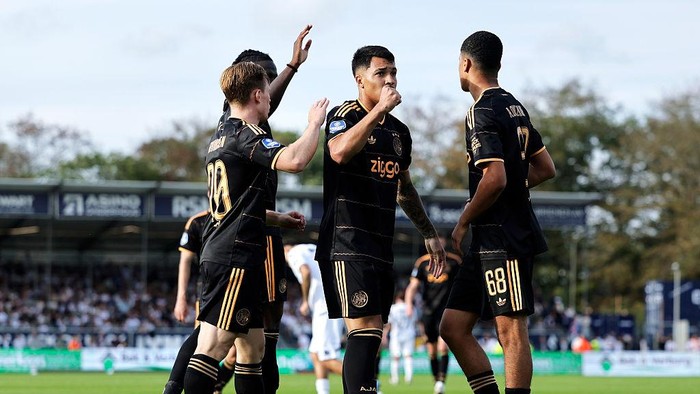 Soccer players in black uniforms celebrate on the field, one raising a hand in a group hug moment during a match.