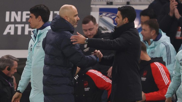 Two coaches shake hands on the sideline during a soccer match.