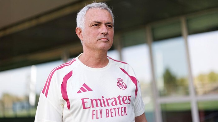 Man with short gray hair wearing a Real Madrid jersey with Emirates logo, standing outdoors.