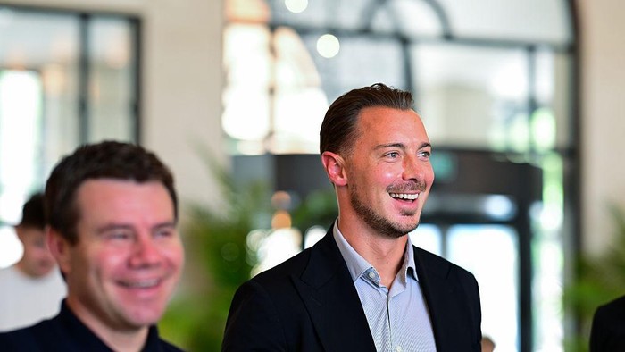 Two smiling men in business attire at an indoor networking event in a modern lobby.