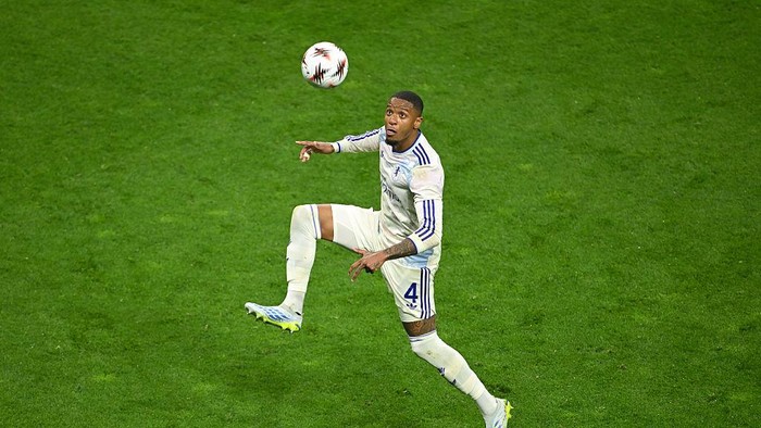 Soccer player in a white uniform mid-air, controlling the ball on a green field during a match.
