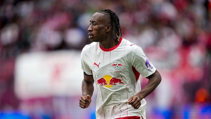 Male soccer player in a white jersey with the Red Bull logo runs on a soccer field during a match, crowd in the blurred background.