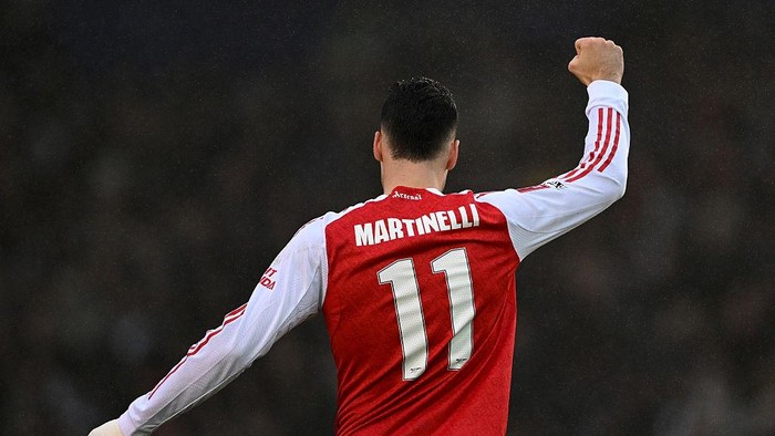 Back view of a soccer player in a red Arsenal jersey with number 11 and the name Martine lli, raising his right fist in celebration.