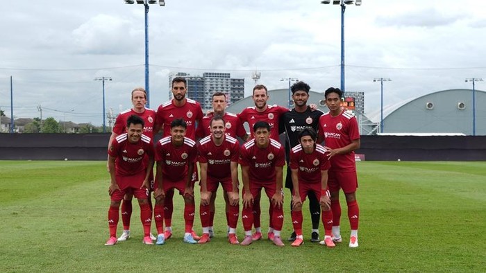 Soccer team in red uniforms posing for a group photo on a grassy field with stadium lights in the background.