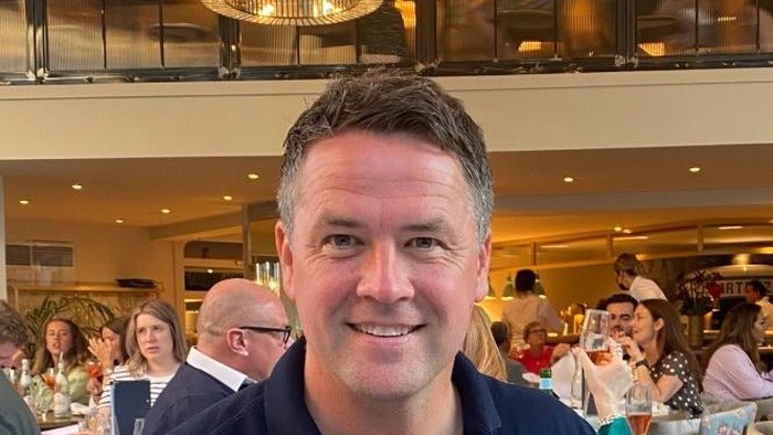 Smiling man in a dark blue shirt in a restaurant, with diners and tables in the background at a group dinner event.