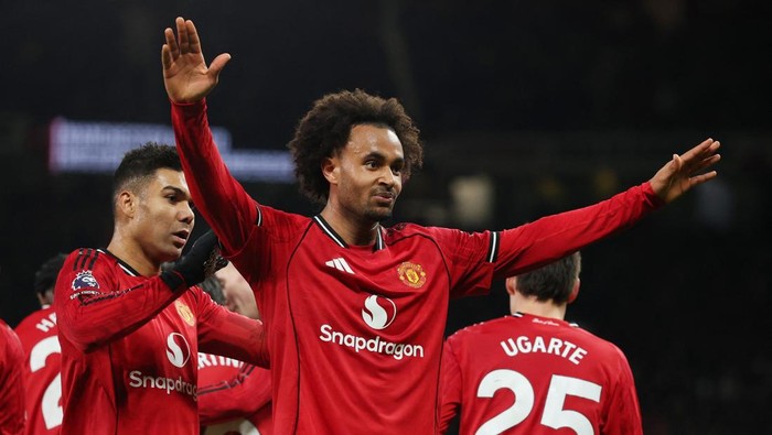 Manchester United players celebrate on the pitch in red jerseys with arms raised.