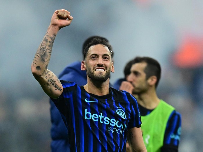 Soccer player in blue-and-black striped jersey raises his fist in celebration on the field.