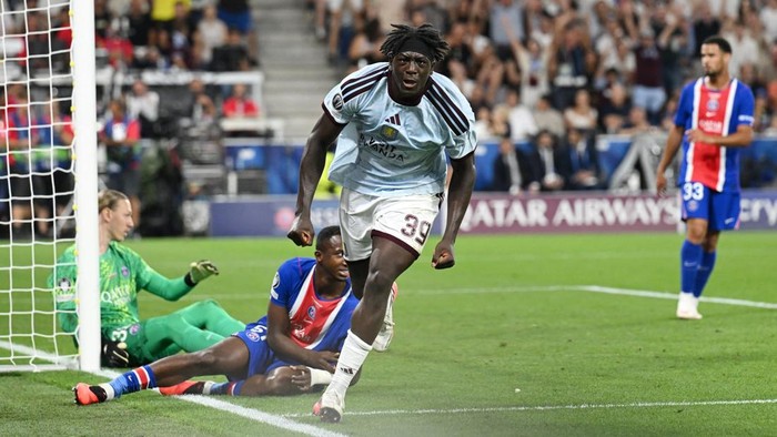 Soccer scene: a forward in white races toward the goal as a defender in blue-red slides in from the right near the net.
