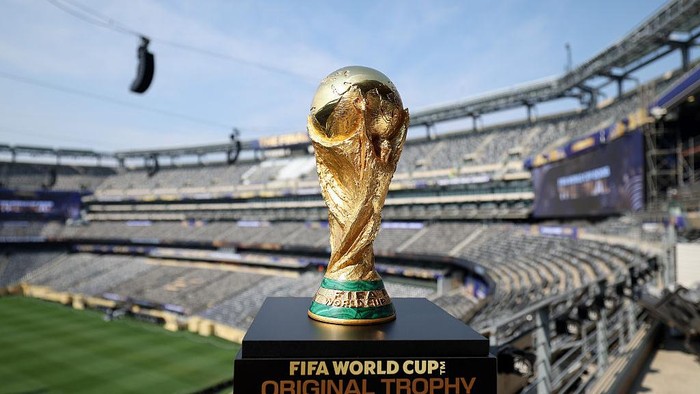 Close-up of the FIFA World Cup trophy on a pedestal in an empty soccer stadium behind it.