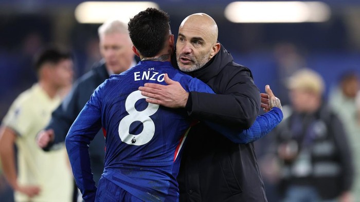 Soccer coach and player hug on the field after a game; the player wears a blue jersey with number 8 and the name Enzo on the back.