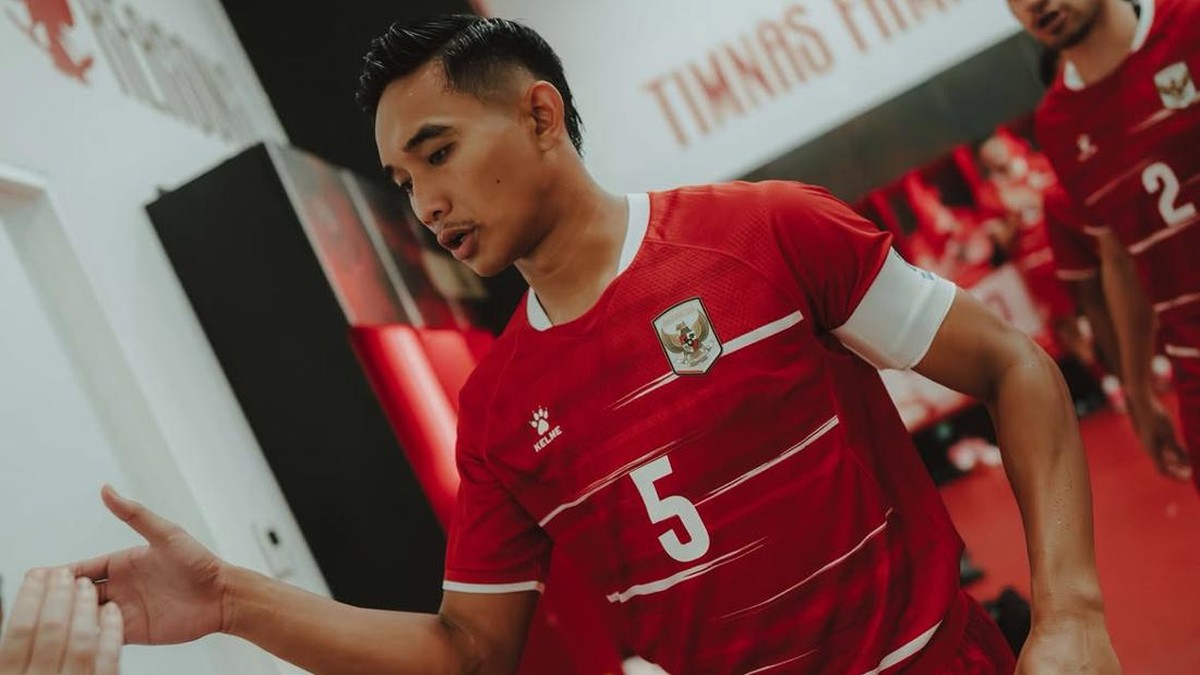 Soccer player in a red jersey with number 5 giving a high-five to a teammate in a locker room.